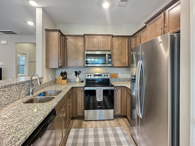 kitchen with stainless steel appliances, light stone countertops, sink, and light hardwood / wood-style flooring