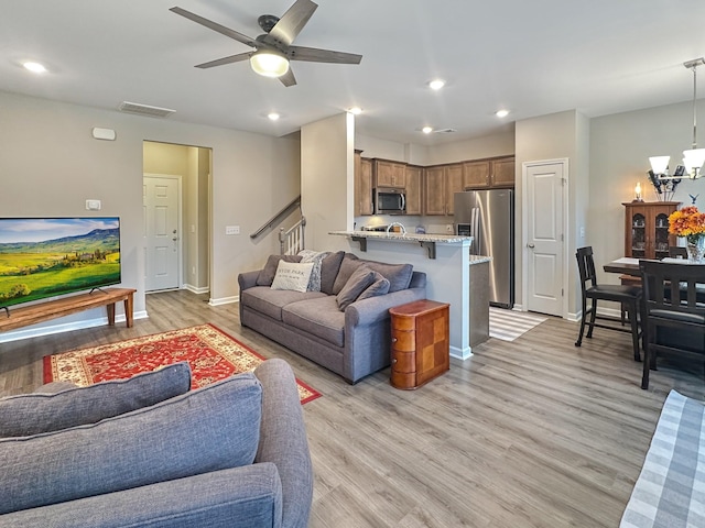 living room featuring ceiling fan with notable chandelier and light hardwood / wood-style flooring