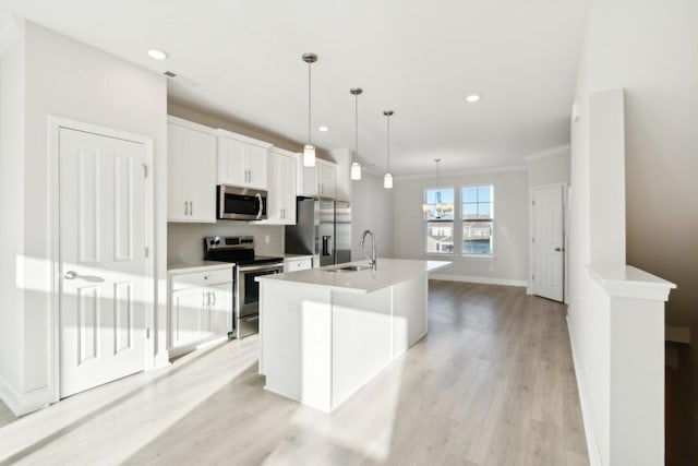 kitchen featuring pendant lighting, white cabinetry, sink, stainless steel appliances, and a center island with sink