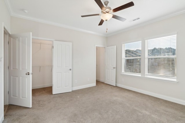 unfurnished bedroom with ceiling fan, ornamental molding, light carpet, a walk in closet, and a closet