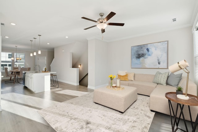 living room with crown molding, sink, ceiling fan, and light hardwood / wood-style flooring