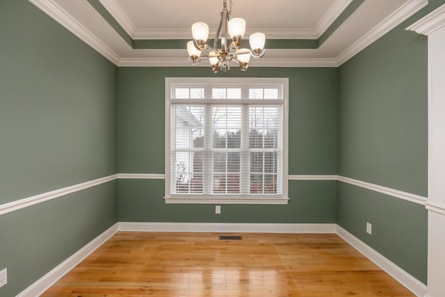 spare room with crown molding, a tray ceiling, a chandelier, and light hardwood / wood-style floors