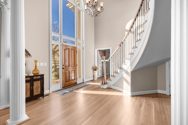 entrance foyer with a wealth of natural light, a chandelier, wood finished floors, and ornate columns