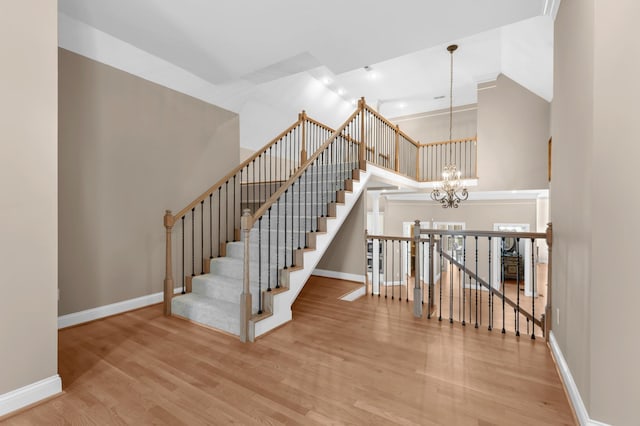 staircase featuring high vaulted ceiling, wood finished floors, baseboards, and a chandelier