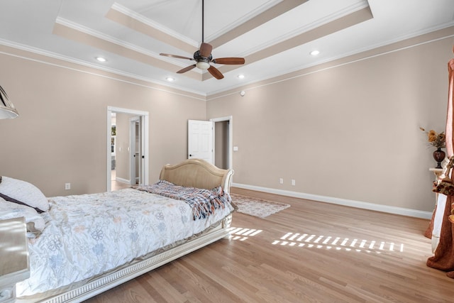 bedroom featuring ornamental molding, a tray ceiling, wood finished floors, recessed lighting, and baseboards