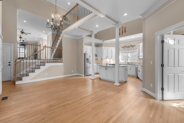 unfurnished living room with stairs, decorative columns, light wood finished floors, and ornamental molding