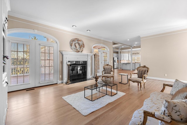 living area featuring visible vents, light wood-style floors, crown molding, a premium fireplace, and baseboards