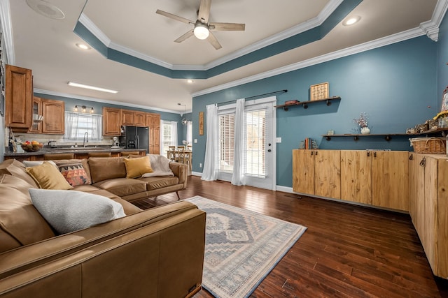 living room featuring ceiling fan, ornamental molding, a tray ceiling, and dark hardwood / wood-style flooring