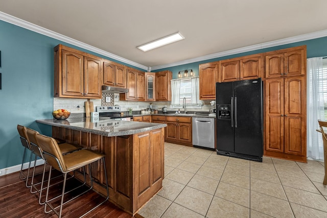 kitchen with appliances with stainless steel finishes, sink, a kitchen bar, ornamental molding, and kitchen peninsula