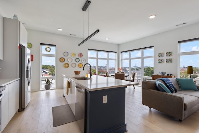 kitchen with decorative light fixtures, sink, white cabinets, a kitchen island with sink, and stainless steel appliances