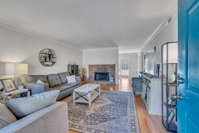 living room featuring a brick fireplace, ornamental molding, and light wood-type flooring