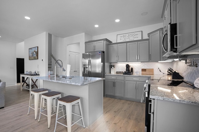 kitchen with stainless steel appliances, light stone countertops, a center island with sink, and a breakfast bar area