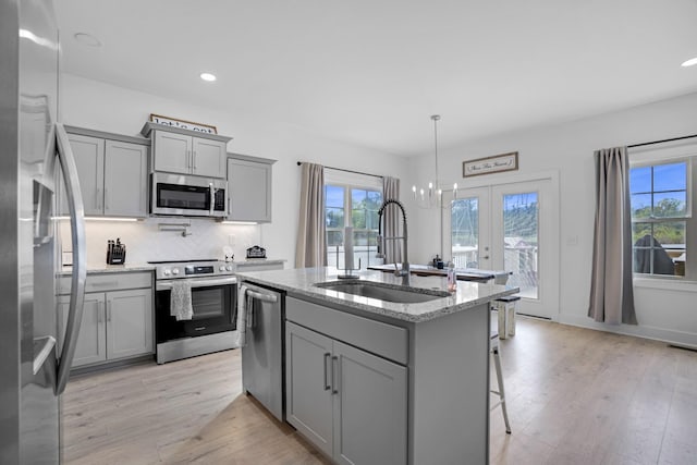 kitchen with sink, hanging light fixtures, appliances with stainless steel finishes, an island with sink, and light stone countertops