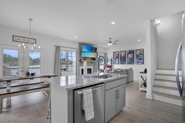 kitchen with an island with sink, sink, hanging light fixtures, light stone counters, and stainless steel appliances