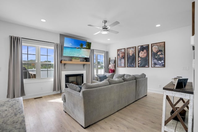 living room with ceiling fan, a large fireplace, and light wood-type flooring