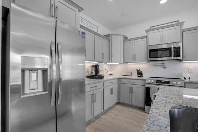 kitchen with light stone counters, appliances with stainless steel finishes, light hardwood / wood-style flooring, and backsplash