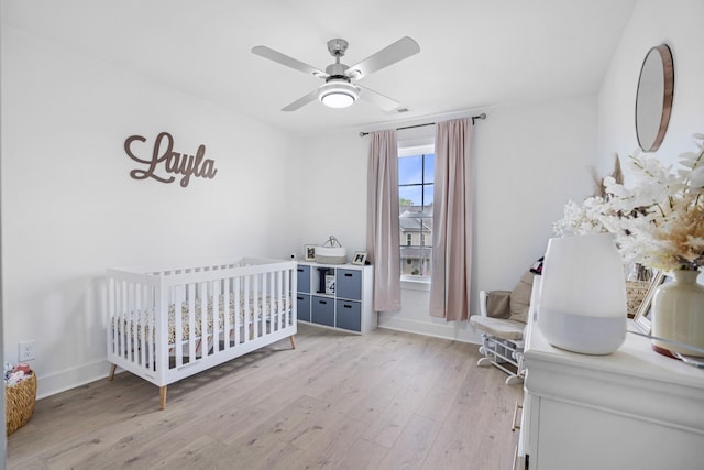 bedroom with a crib, ceiling fan, and light hardwood / wood-style floors