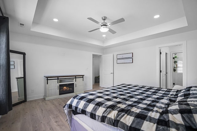 bedroom with a tray ceiling, light hardwood / wood-style floors, and ceiling fan