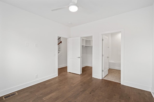 unfurnished bedroom featuring ceiling fan, ensuite bathroom, wood-type flooring, a spacious closet, and a closet