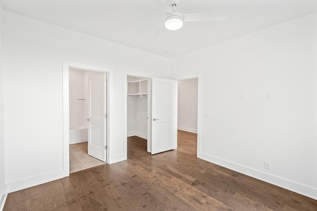 unfurnished bedroom with ceiling fan, ensuite bathroom, wood-type flooring, a spacious closet, and a closet