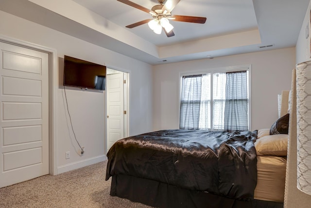 carpeted bedroom with a raised ceiling and ceiling fan