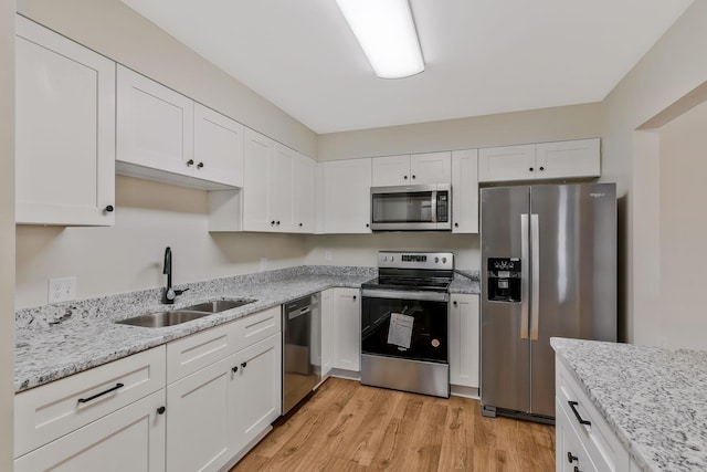 kitchen featuring sink, stainless steel appliances, light hardwood / wood-style floors, light stone countertops, and white cabinets