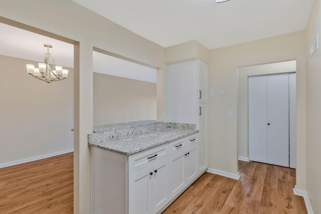 kitchen with pendant lighting, white cabinetry, light stone countertops, an inviting chandelier, and light hardwood / wood-style flooring