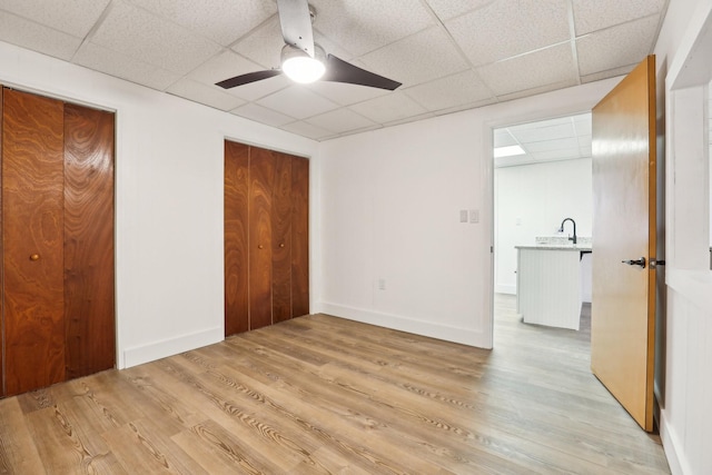 unfurnished bedroom featuring ceiling fan, a paneled ceiling, sink, and light hardwood / wood-style floors