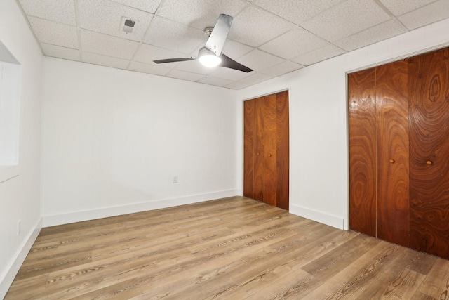 unfurnished bedroom featuring multiple closets, ceiling fan, a drop ceiling, and light wood-type flooring