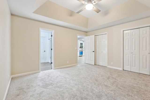 unfurnished bedroom featuring a raised ceiling, two closets, and light colored carpet