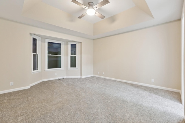 spare room with a tray ceiling, carpet floors, and ceiling fan