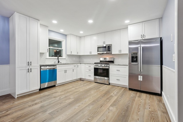 kitchen featuring sink, tasteful backsplash, light wood-type flooring, stainless steel appliances, and white cabinets