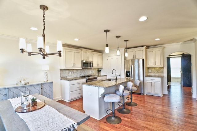 kitchen featuring appliances with stainless steel finishes, decorative light fixtures, an island with sink, sink, and dark stone countertops