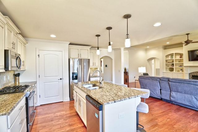 kitchen featuring light stone counters, stainless steel appliances, decorative light fixtures, and an island with sink