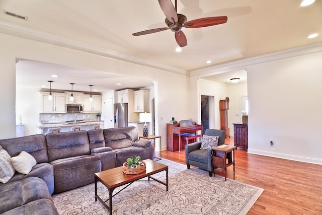 living room with crown molding, light hardwood / wood-style floors, and ceiling fan