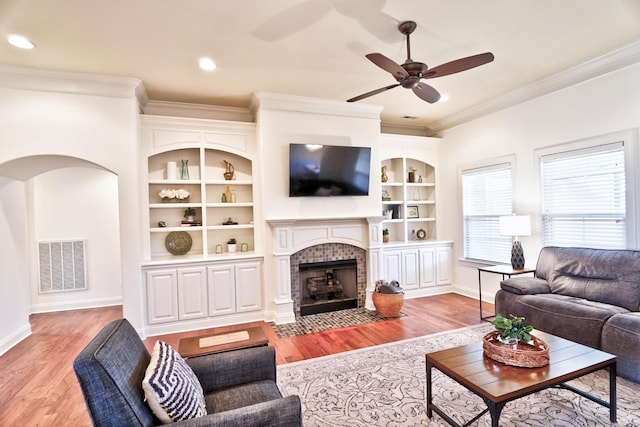 living room with a tiled fireplace, built in features, light hardwood / wood-style flooring, and ornamental molding