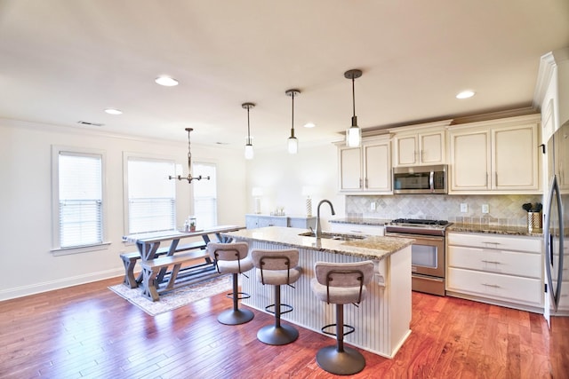 kitchen featuring decorative light fixtures, sink, stainless steel appliances, light stone countertops, and a center island with sink