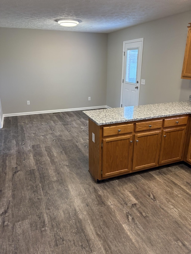 kitchen featuring light stone counters, dark wood-type flooring, kitchen peninsula, and a textured ceiling