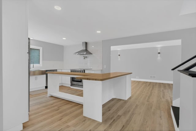 kitchen featuring appliances with stainless steel finishes, a breakfast bar, butcher block countertops, white cabinets, and wall chimney range hood