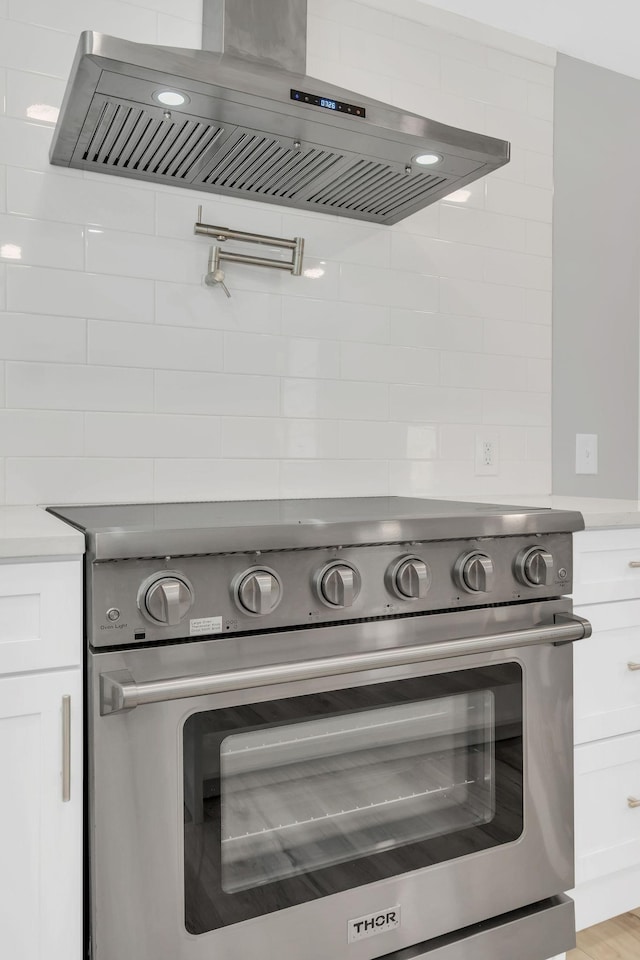 details with white cabinetry, exhaust hood, and stainless steel range