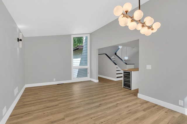 unfurnished living room featuring wine cooler, an inviting chandelier, and light hardwood / wood-style floors