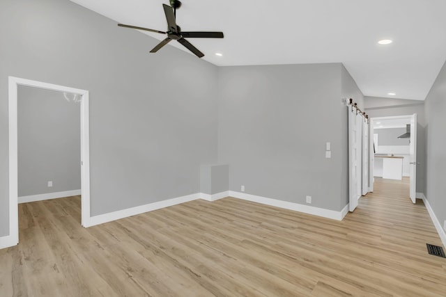 unfurnished living room with a barn door, lofted ceiling, ceiling fan, and light hardwood / wood-style flooring