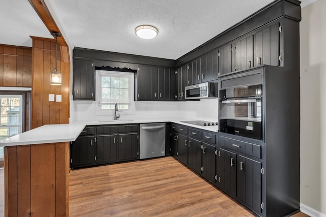 kitchen featuring decorative light fixtures, black appliances, sink, kitchen peninsula, and light hardwood / wood-style flooring