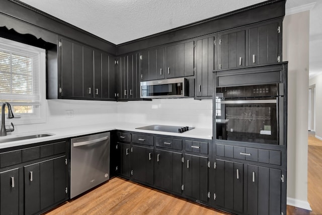 kitchen with sink, appliances with stainless steel finishes, light hardwood / wood-style floors, a textured ceiling, and decorative backsplash