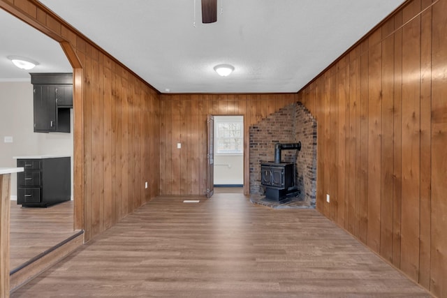 unfurnished living room with crown molding, light hardwood / wood-style floors, wood walls, and a wood stove