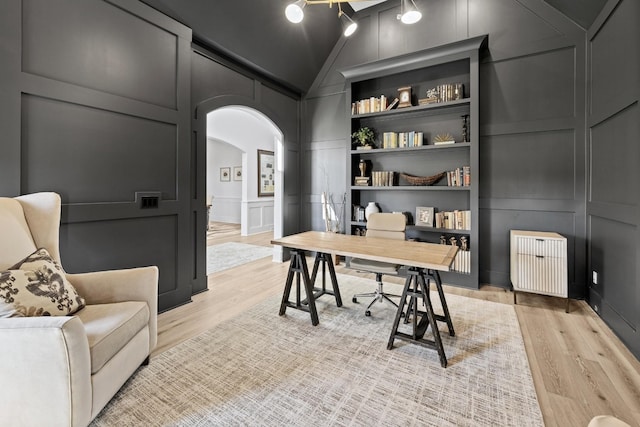 office with built in shelves, lofted ceiling, radiator heating unit, and light wood-type flooring