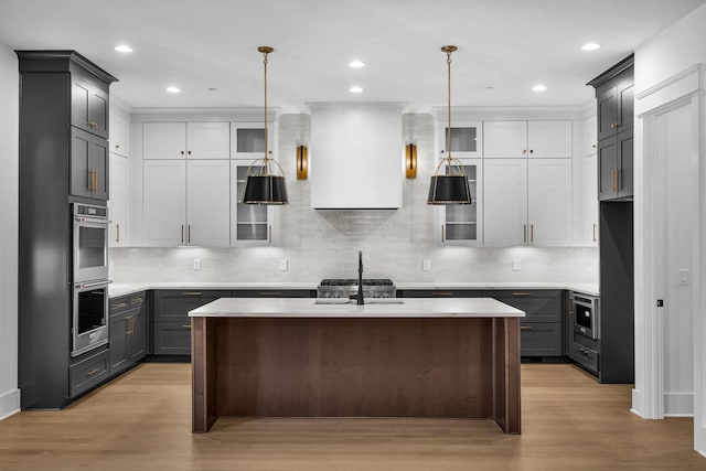 kitchen with sink, wall chimney range hood, gray cabinetry, an island with sink, and decorative light fixtures