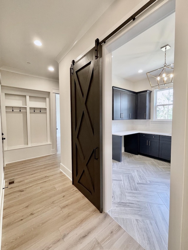 hallway featuring crown molding, a barn door, light parquet floors, and a notable chandelier