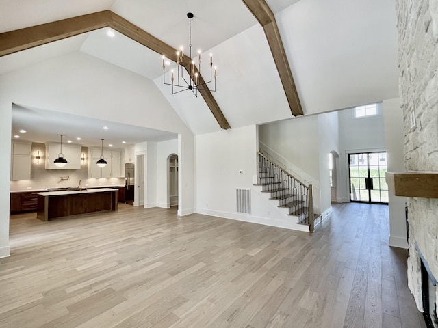 unfurnished living room with beamed ceiling, high vaulted ceiling, a stone fireplace, and light hardwood / wood-style floors