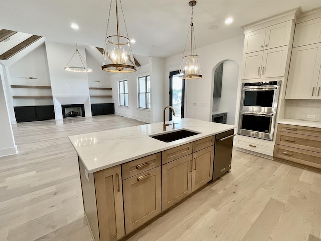 kitchen featuring sink, double oven, hanging light fixtures, a spacious island, and light stone countertops